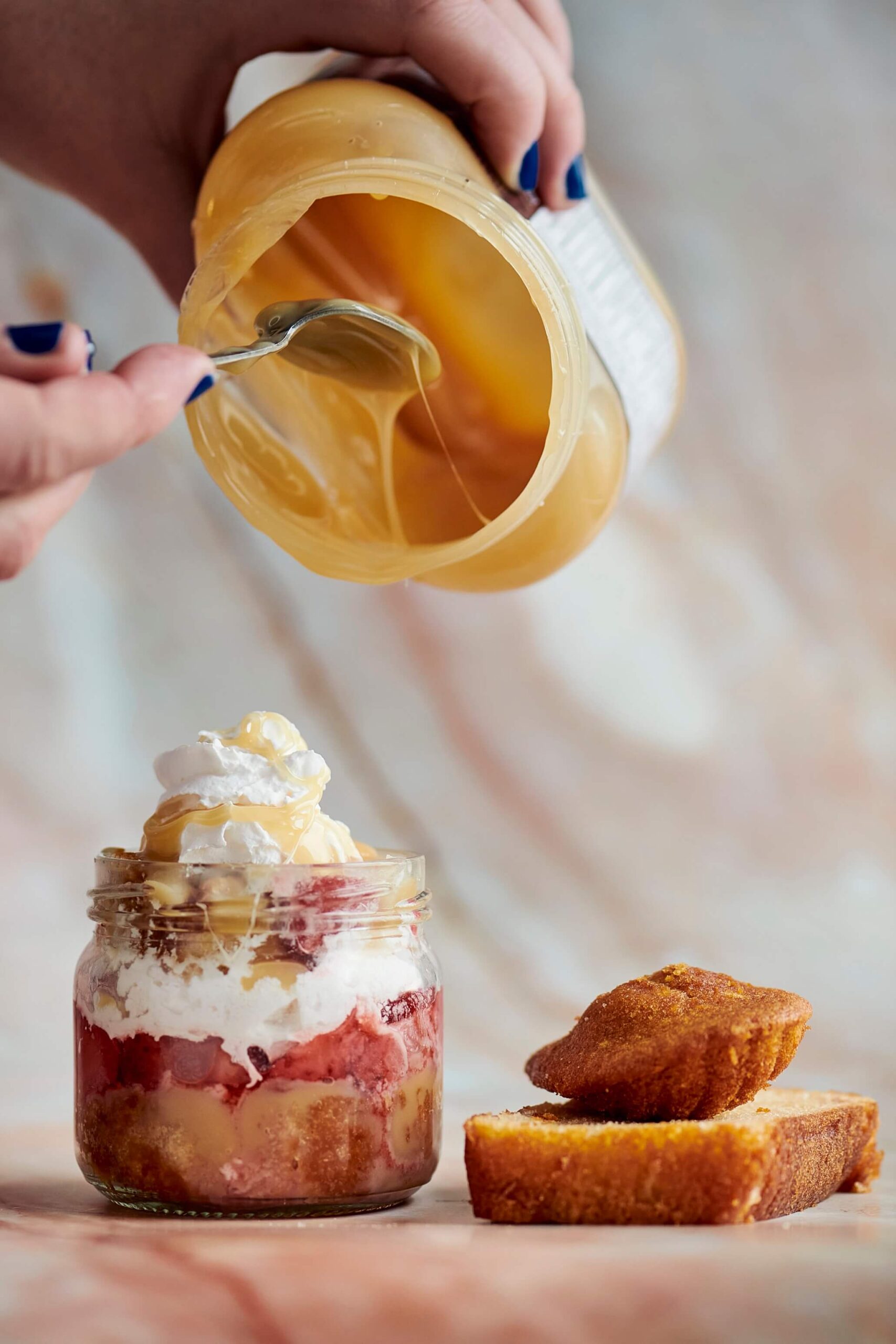 Bagatelle vide-frigo vue de côté, dans un petit pot en verre. On voit les étages de gâteau madeleine émietté, entre-coupé de crème, de caramel et de fraises tranchées